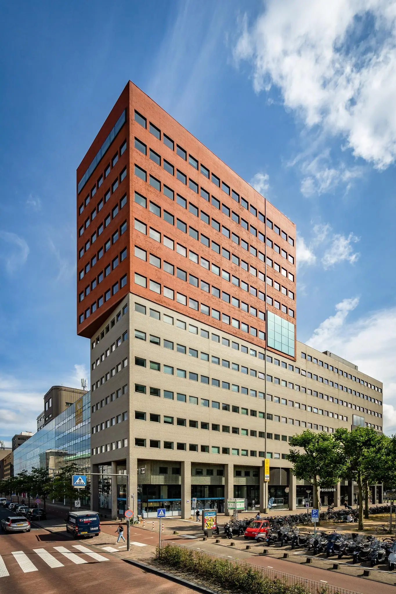 Kantoorgebouw aan het Johanna Westerdijkplein met opvallende roodkleurige bovenverdiepingen en beige onderbouw, onder een blauwe lucht.